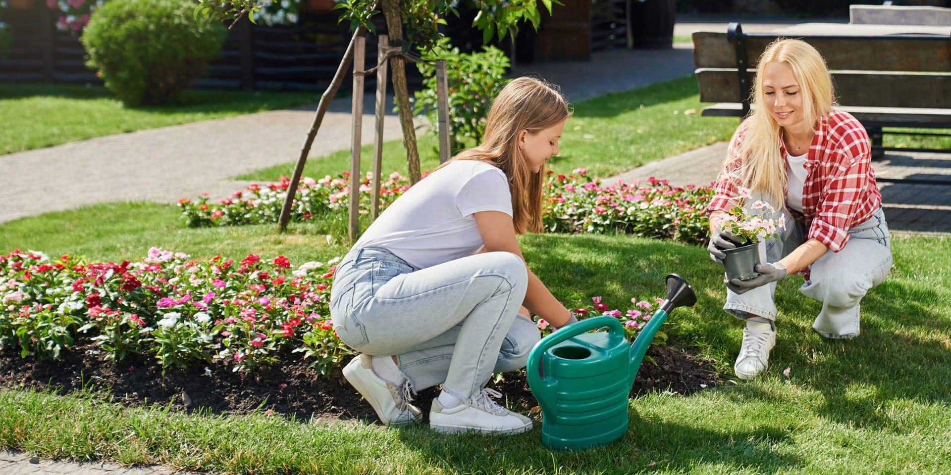 Mother and daughter in gloves planting flowers at garden